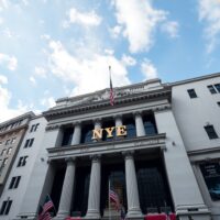 New York Stock Exchange building facade on Wall Street under partly cloudy sky