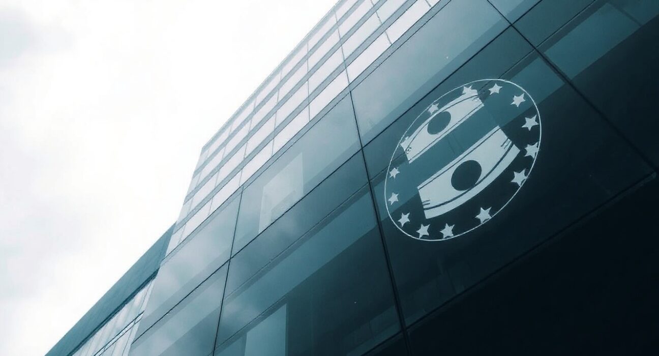 European Central Bank headquarters in Frankfurt on a cloudy day, with oil barrel reflection symbolizing rate hike risk.