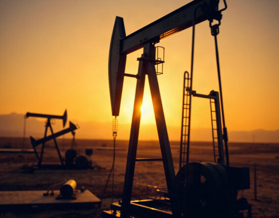 Crude oil pump jack silhouetted against sunset sky in oil field
