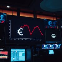 Digital trading board showing declining EUR/USD exchange rate chart in a dimly lit foreign exchange trading room.