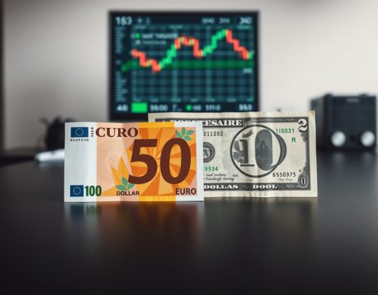 Euro and US Dollar banknotes on a desk with a financial chart in the background.