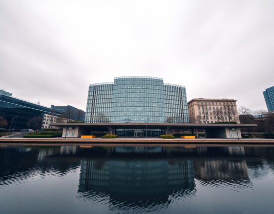 European Central Bank headquarters in Frankfurt on a cloudy day, reflecting in the Main River.