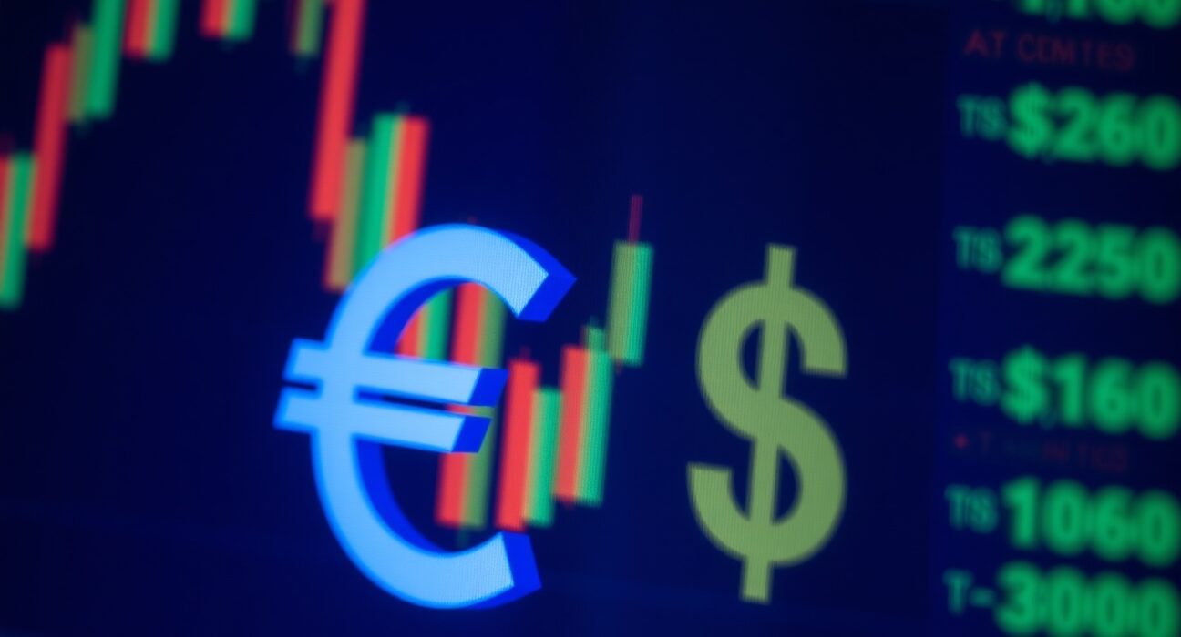 Euro and US dollar symbols on a financial trading screen with market charts in background.