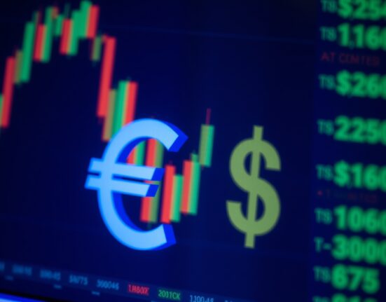 Euro and US dollar symbols on a financial trading screen with market charts in background.