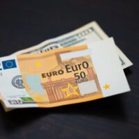 Close-up of a Euro banknote partially overlapping a US dollar bill on a dark desk, representing currency exchange rates.