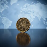 Euro coin standing upright on a reflective surface with a blurred world map background.