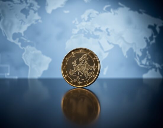Euro coin standing upright on a reflective surface with a blurred world map background.