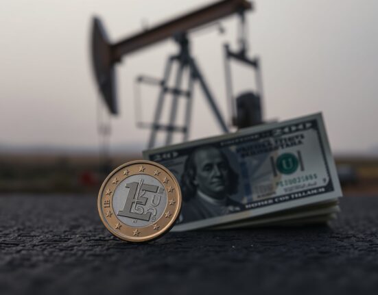 Euro coin and US dollar bill on dark surface with oil pump jack silhouette in background