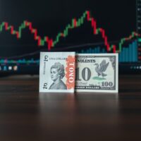 British Pound and US Dollar banknotes on a trader's desk with a chart in the background.