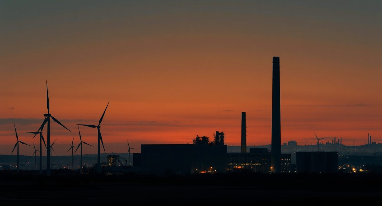 Industrial landscape in Germany with power plant and wind turbines at dusk, illustrating energy crisis and economic impact.