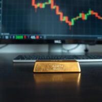Gold bar on wooden surface with financial chart showing downward trend in background