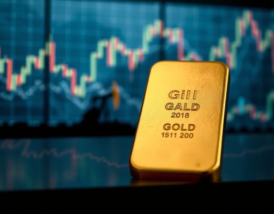 Gold bar on reflective surface with blurred financial charts and oil derrick in background