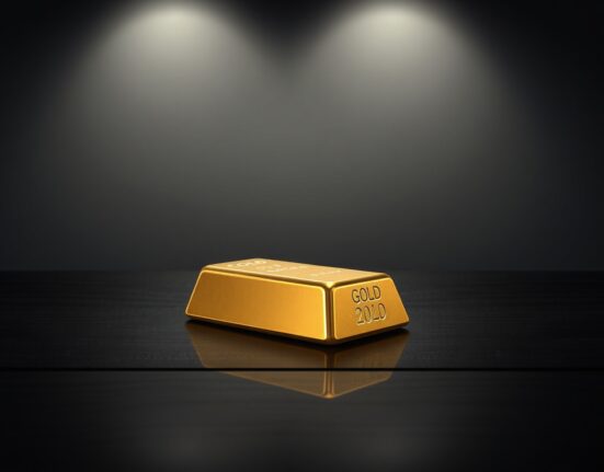 Gold bar on a dark surface reflecting a declining price chart, representing gold hits four-week low due to firmer US Dollar and oil-driven inflation.