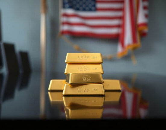 Gold bullion bars stacked with a blurred American flag in background, representing gold prices and Federal Reserve policy