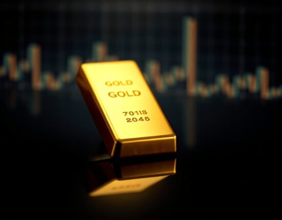 Gold bar on reflective surface with subtle market chart overlay