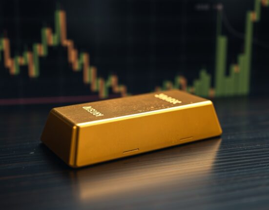 Gold bar on wooden surface with blurred financial charts in background, representing gold price analysis.