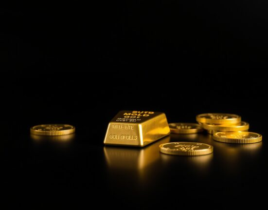 Gold bars and coins on a dark surface representing precious metal investment and market analysis.
