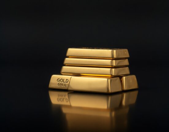 Stacked gold bars on dark reflective surface with soft lighting for market analysis article.