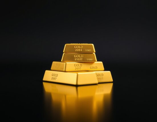 Close-up of gold bars on a dark reflective surface representing safe-haven demand.