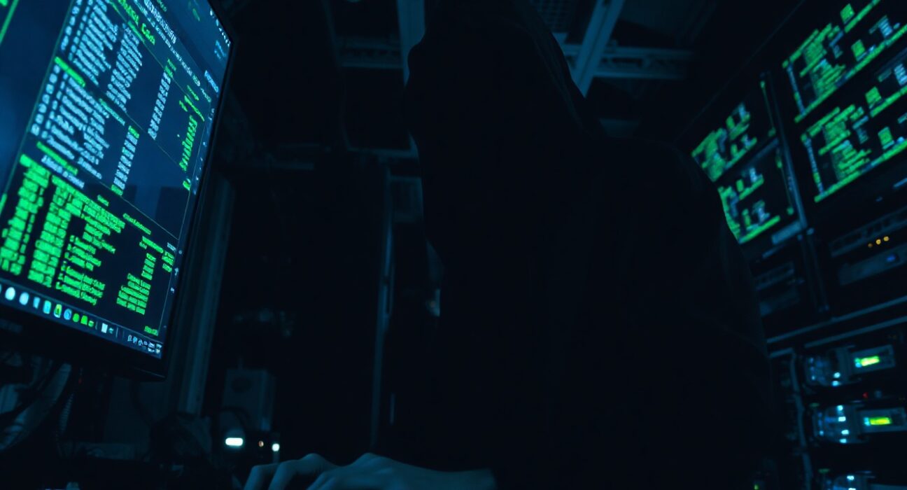 Hooded figure in a dark server room using a computer to launder cryptocurrency through Tornado Cash