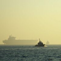 Aerial view of the Strait of Hormuz with a tanker and military vessel, illustrating heightened tensions.