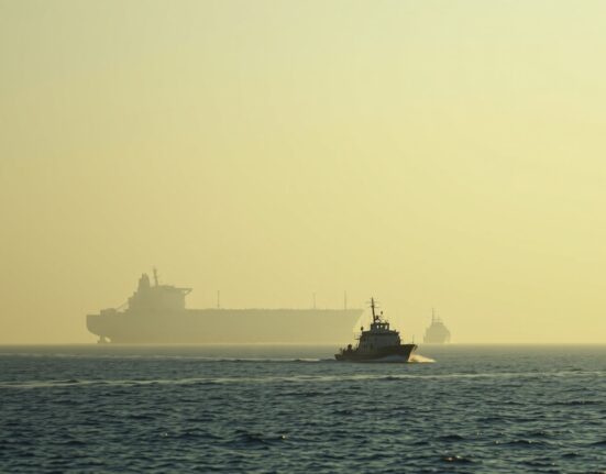 Aerial view of the Strait of Hormuz with a tanker and military vessel, illustrating heightened tensions.