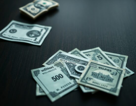 Indian rupee banknotes scattered on a dark surface with a US dollar bill at the edge, representing currency depreciation.