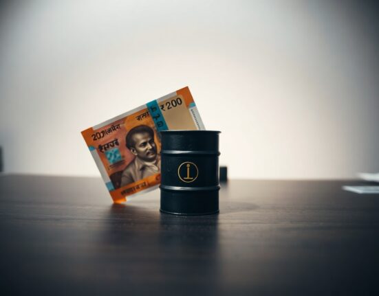 Indian Rupee notes and a small oil barrel on a desk representing currency and oil price dynamics