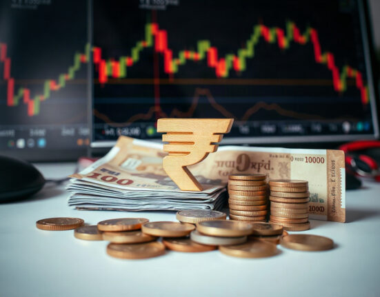 Indian Rupee currency notes and coins on a desk with financial charts in background