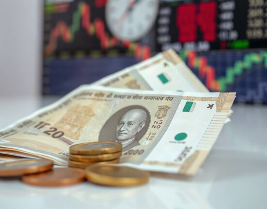 Indian Rupee banknotes and coins on a table with a blurred financial chart in the background