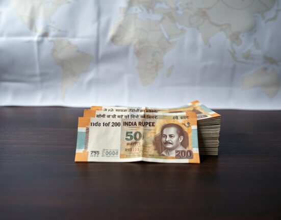 Indian Rupee banknotes on a table with a world map showing the Strait of Hormuz in the background