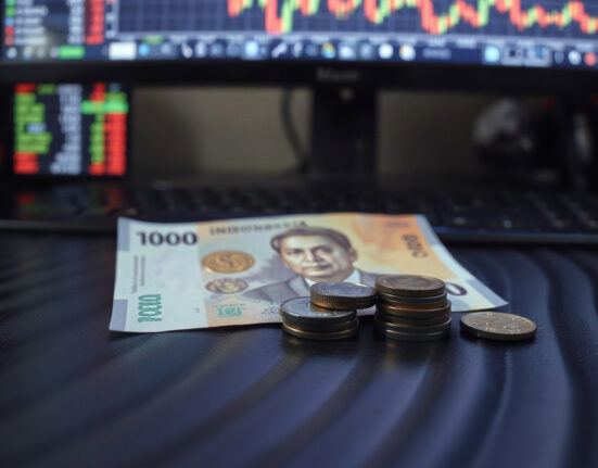 Indonesian rupiah banknotes and coins on a dark surface with a financial chart in the background