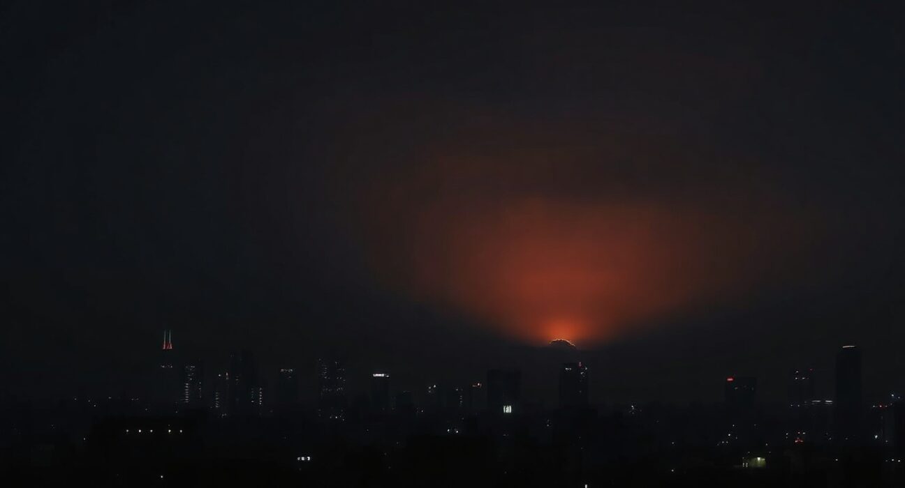 Night skyline of Tehran with faint orange glow on horizon after reported strikes