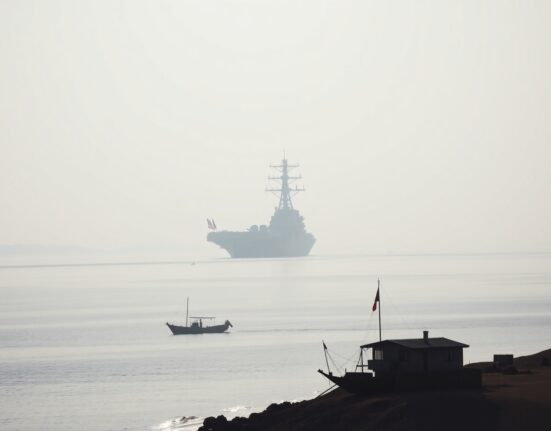 A US naval vessel in the Persian Gulf with an Iranian coastline in the foreground, illustrating regional military tensions.