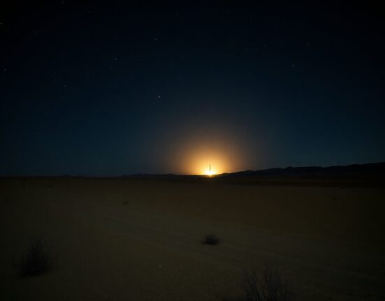 Nighttime desert landscape with a distant glow on the horizon, representing a missile launch or explosion.