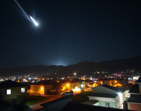 Night sky over a city with an interceptor missile streaking upward toward a distant explosion