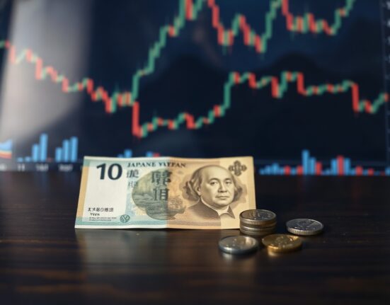 Japanese yen banknotes and coins on a wooden surface with financial charts in the background.