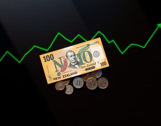New Zealand Dollar banknotes and coins with an upward trending graph, representing positive economic outlook.