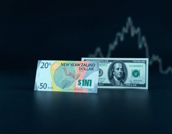 New Zealand and US dollar banknotes on a dark surface with a subtle chart in the background