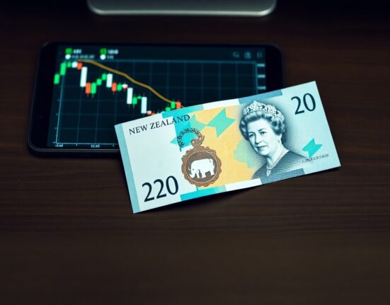 New Zealand dollar banknote on a desk with a financial chart showing a downward trend