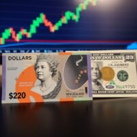 New Zealand Dollar and US Dollar banknotes on a trading desk with a forex chart in the background.