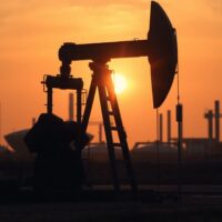 Oil pumpjack at sunset with refinery and city traffic background illustrating conflicting demand signals