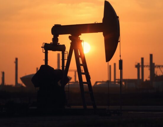 Oil pumpjack at sunset with refinery and city traffic background illustrating conflicting demand signals