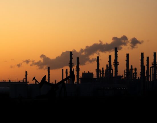 Oil refinery at dusk with pumpjack in foreground, symbolizing rising crude prices due to geopolitical risk.