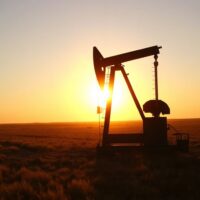 Oil pumpjack silhouetted at sunset in an oil field, representing crude oil supply and market conditions.