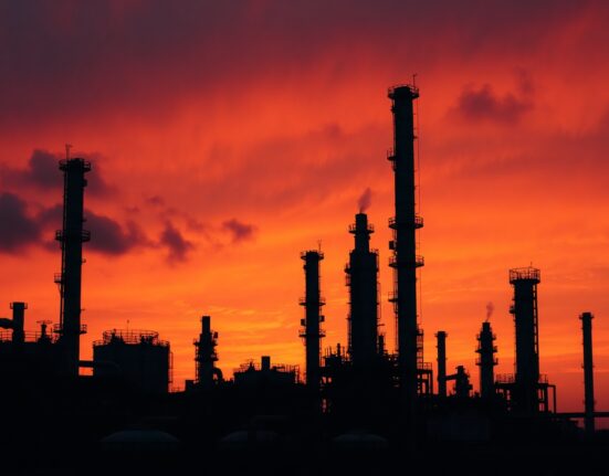 Oil refinery at dusk with smoky sky, symbolizing energy market disruption from Iran conflict