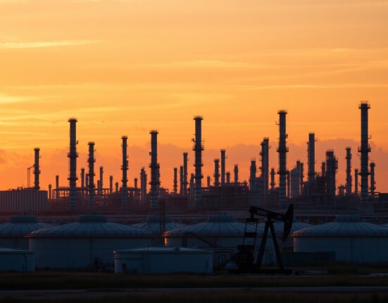 Oil refinery at sunset with pumpjack silhouette, representing energy market volatility