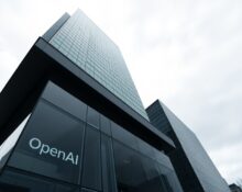 Exterior of a modern glass office building with OpenAI logo visible on ground floor.