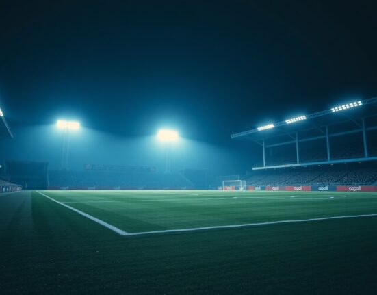 A football stadium lit by floodlights at night, empty pitch before a match.