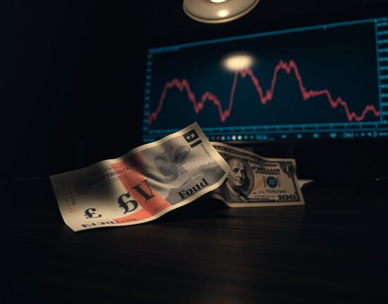 British Pound and US Dollar banknotes on a desk with a downward chart in the background